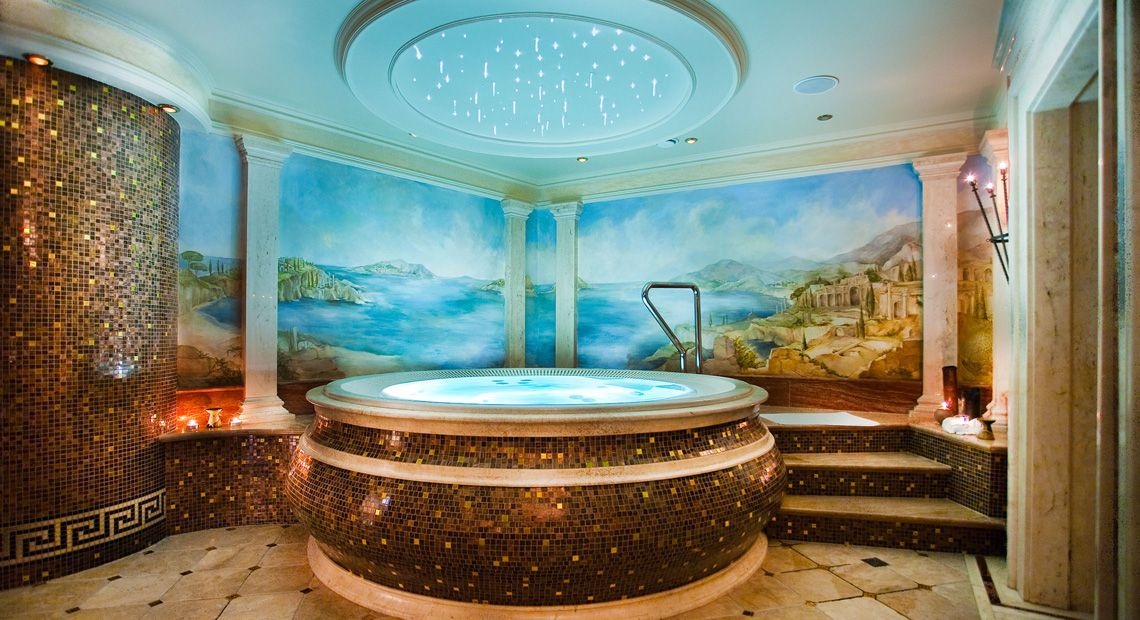 Luksusowa wanna jacuzzi z mozaikową obudową, otoczona kolumnami i malowidłami ściennymi z motywem śródziemnomorskim; sufit podświetlany gwiazdami, tworzący atmosferę relaksu w SPA.
