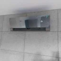 Nowoczesny klimatyzator Rotenso Versu Series w srebrnej obudowie, jeszcze z folią ochronną, zamontowany na szarej ścianie z efektem betonu.