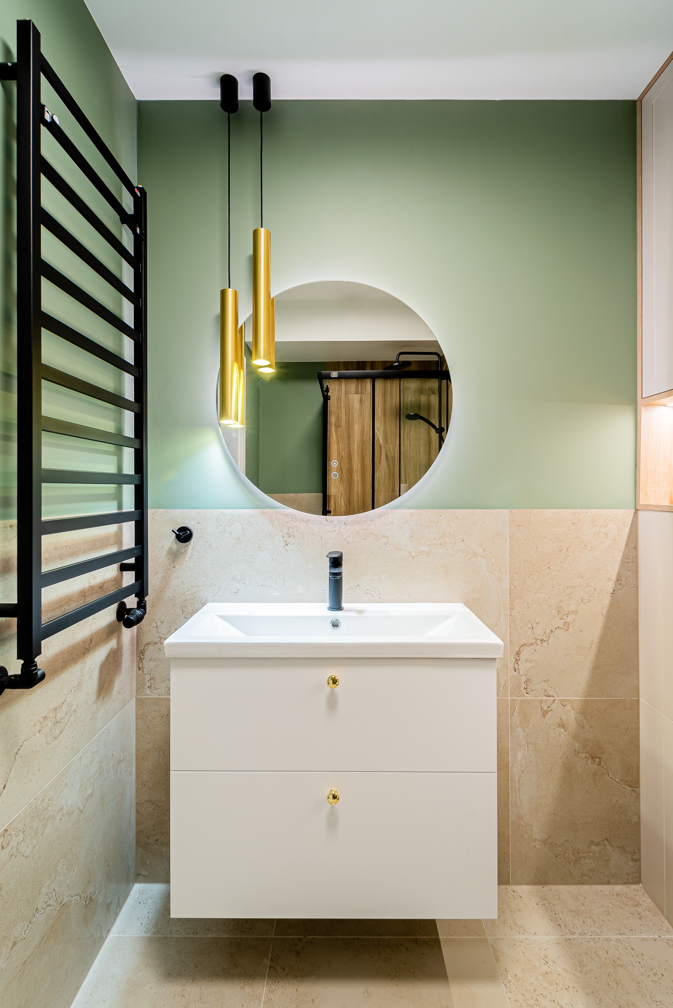 Nowoczesna łazienka z umywalką na szafce, okrągłym lustrem z podświetleniem LED i złotymi lampami wiszącymi na tle pistacjowej ściany i beżowych płytek.