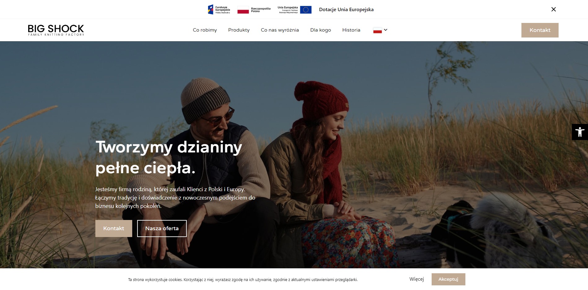 Strona internetowa firmy Big Shock prezentująca parę w dzianinowych ubraniach na tle plaży i wydm, z hasłem 'Tworzymy dzianiny pełne ciepła' oraz logo firmy w lewym górnym rogu.