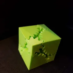 Jasnozielony, drukowany w 3D sześcian z zazębiającymi się elementami przypominającymi koła zębate, na ciemnym tle.