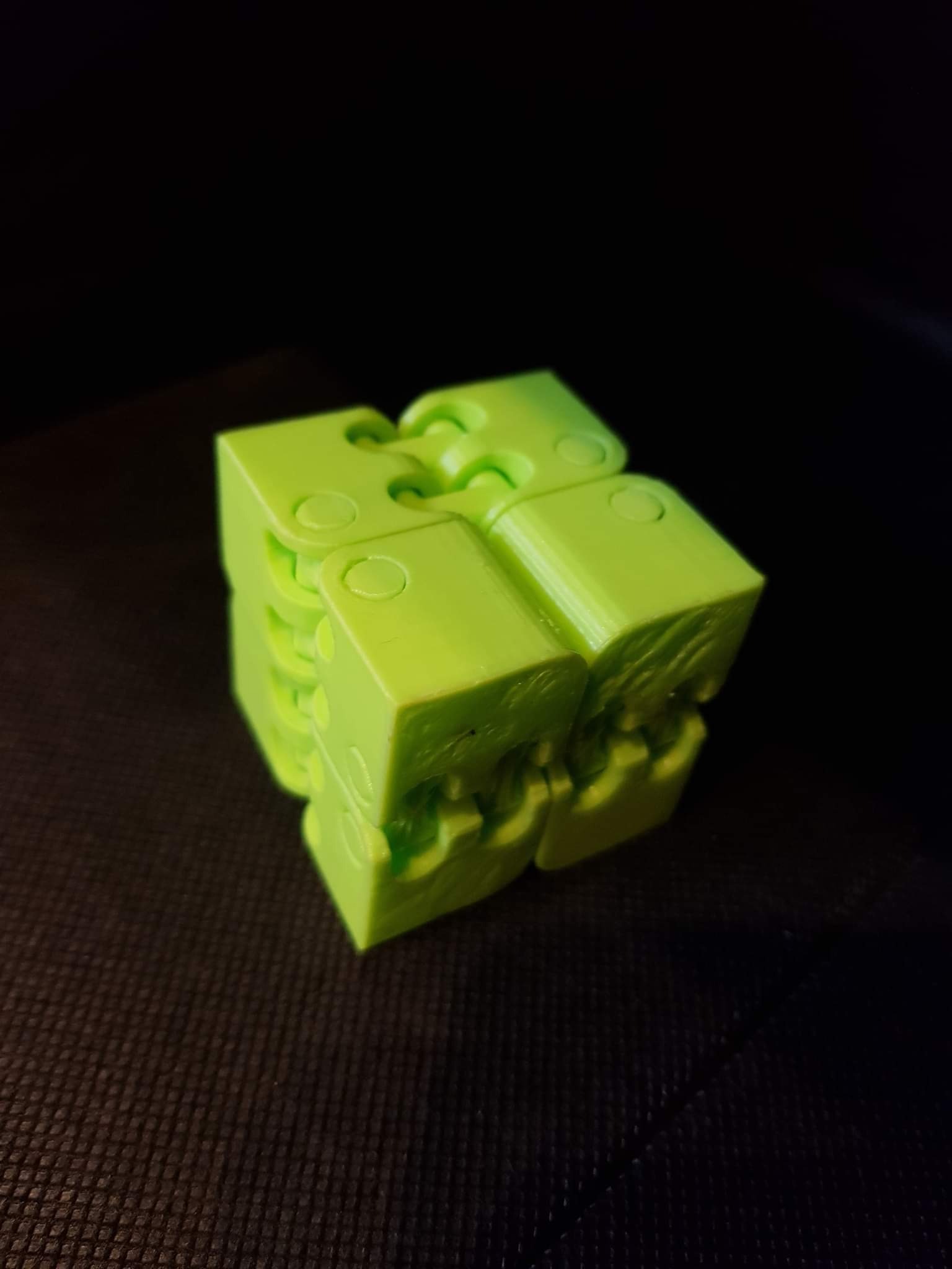 Jasnozielony, modułowy sześcian z tworzywa sztucznego na ciemnym tle, ukazujący konstrukcję z połączeniami zawiasowymi.