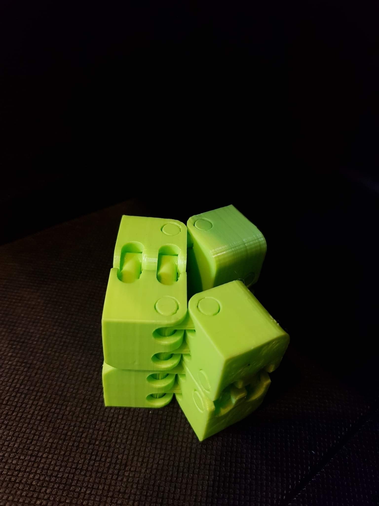 Jasnozielony, przegubowy model z tworzywa sztucznego, prawdopodobnie wydrukowany w 3D, na ciemnym tle. Widoczne warstwy druku.