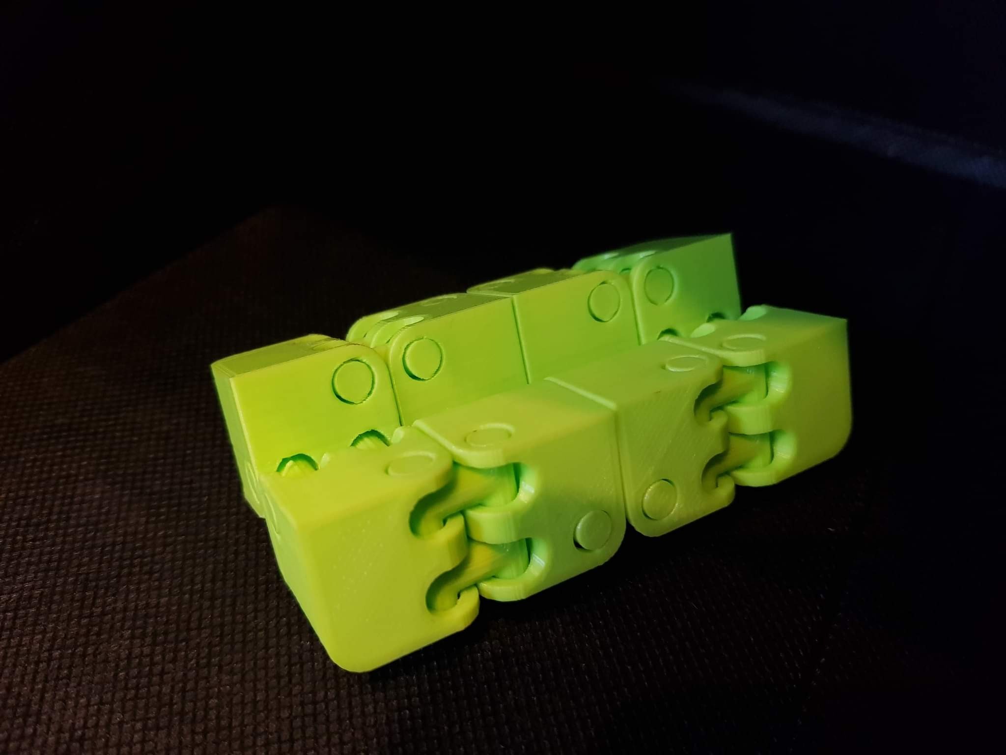 Żółto-zielony, przegubowy model 3D wydrukowany na drukarce 3D, leżący na ciemnej powierzchni.