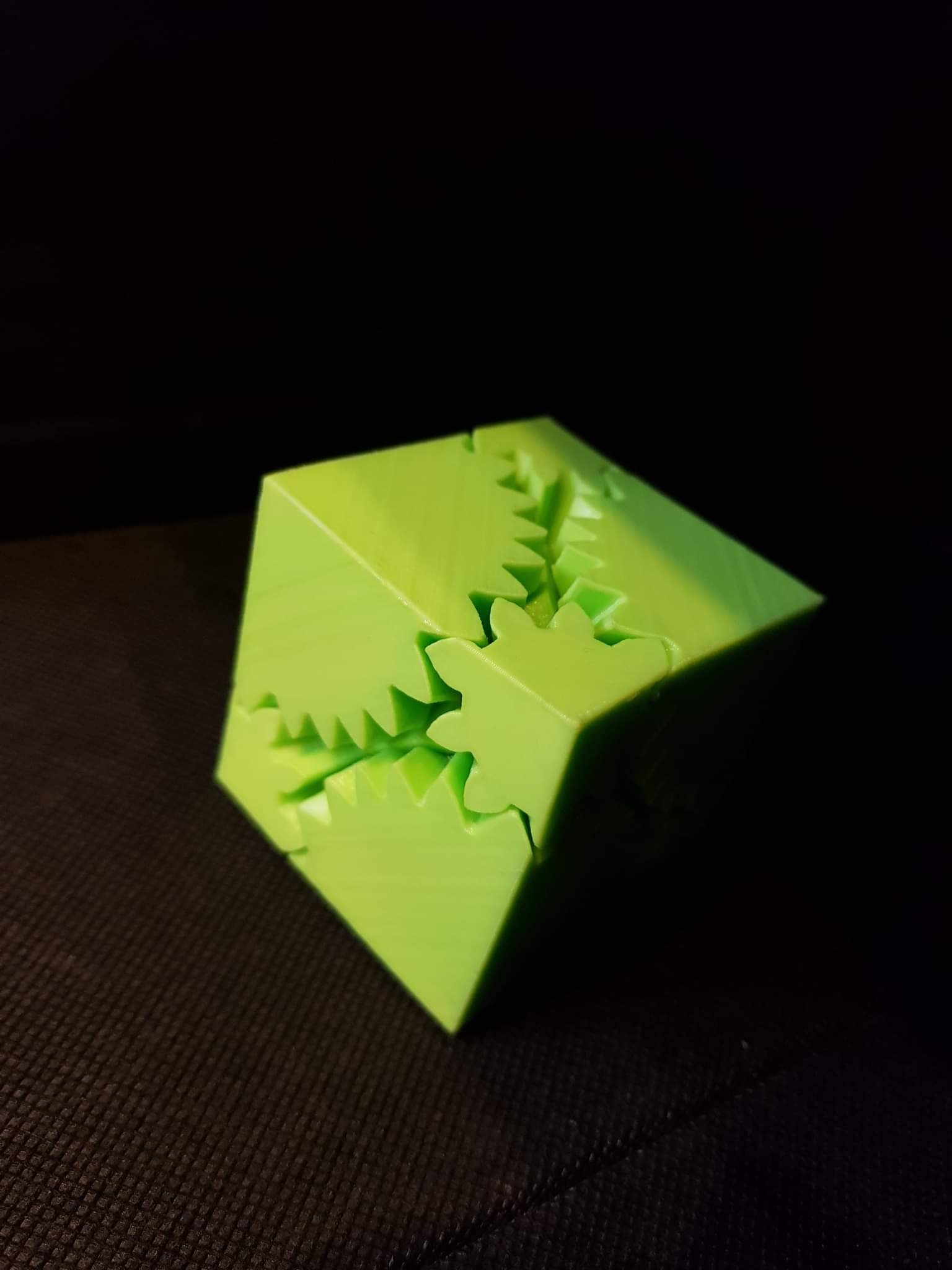 Jasnozielony, sześcienny model z elementami przypominającymi zębatki, wydrukowany w 3D, na ciemnym tle.