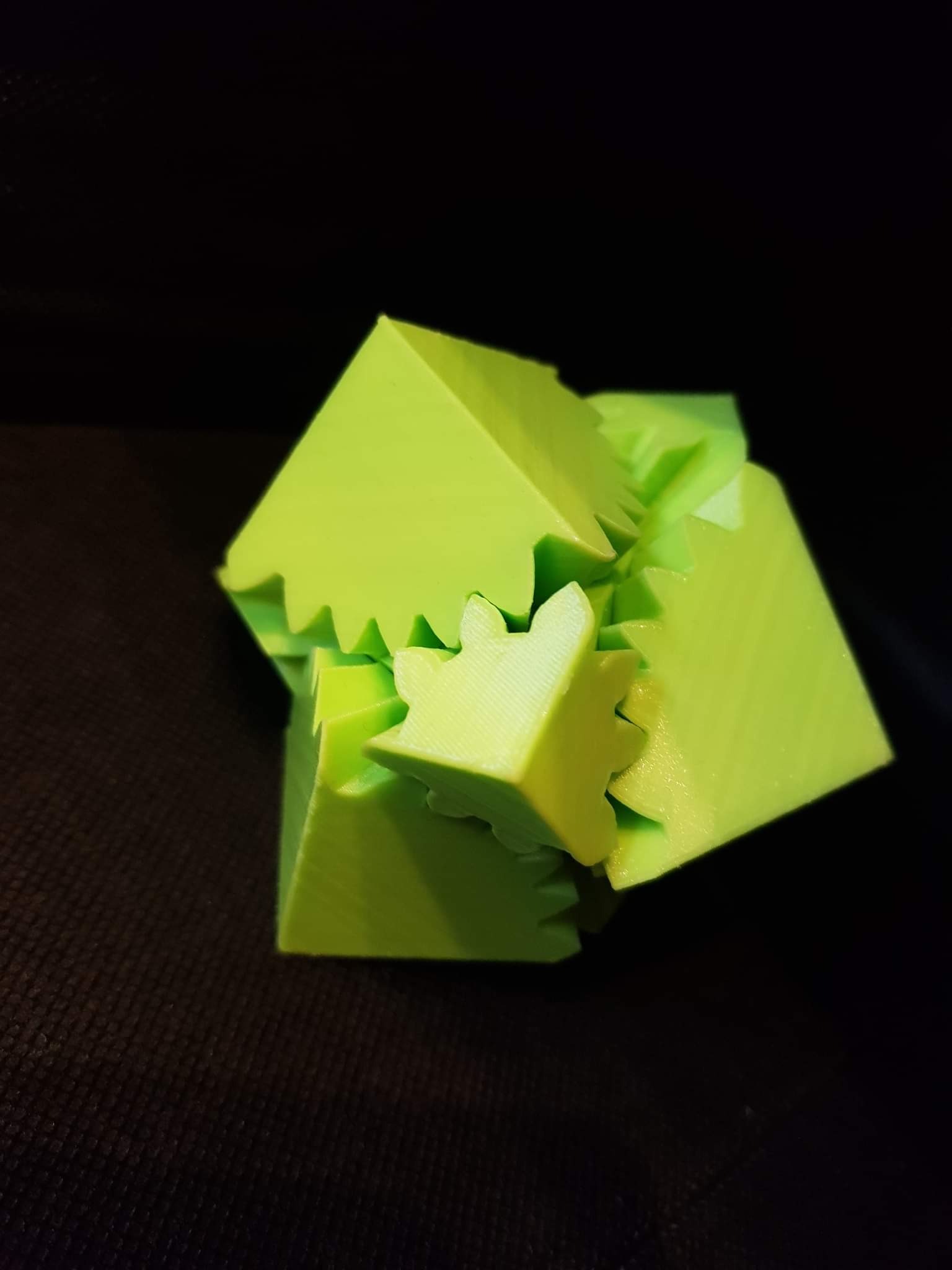 Jasnozielony model 3D złożony z kostek z zębatymi krawędziami, wydrukowany na drukarce 3D, leżący na ciemnym tle.