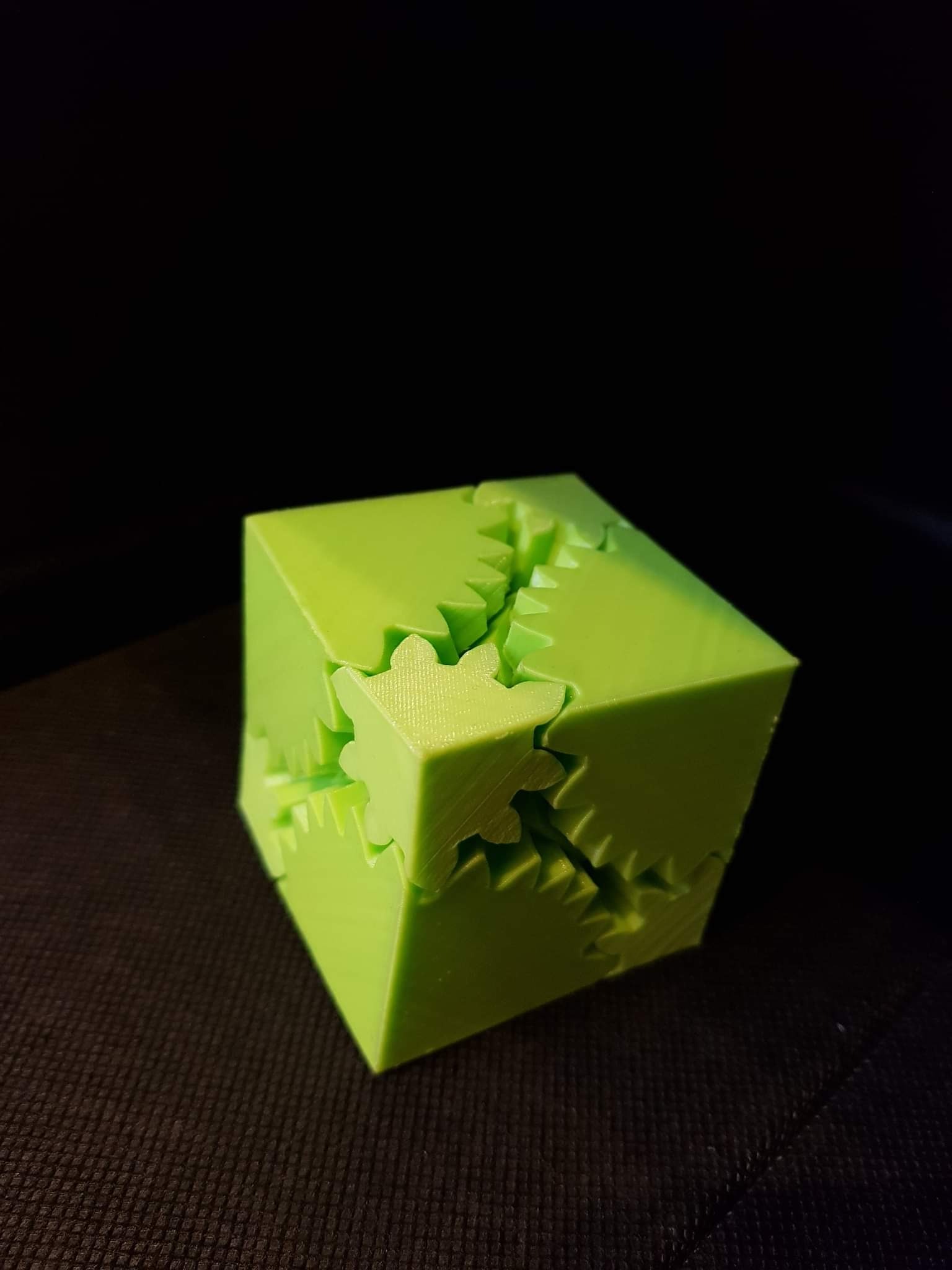 Jasnozielony, drukowany w 3D sześcian z zazębiającymi się elementami przypominającymi koła zębate, na ciemnym tle.