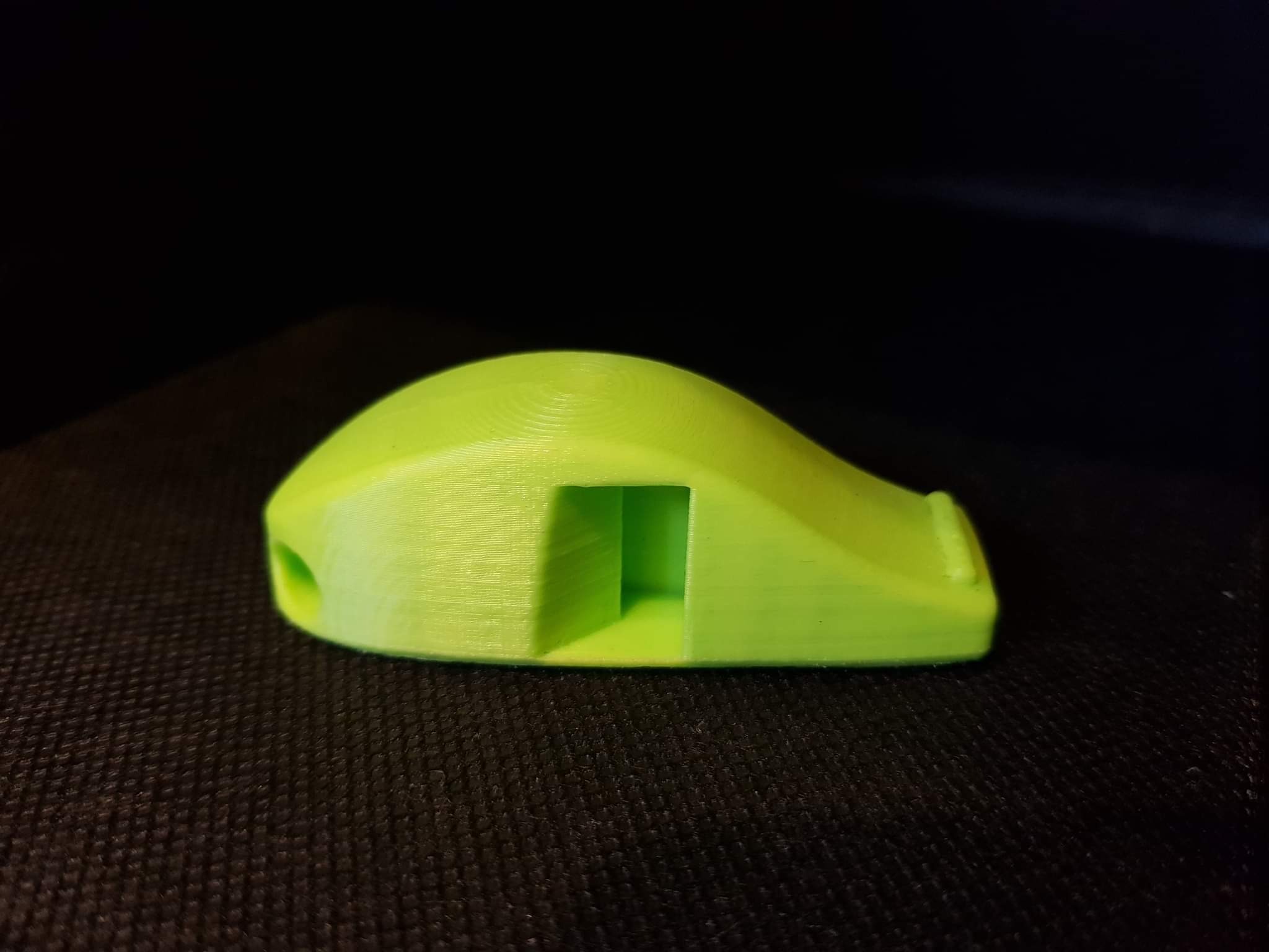 Żółty gwizdek, wydrukowany w 3D, leży na ciemnej, teksturowanej powierzchni. Widoczne warstwy druku 3D.