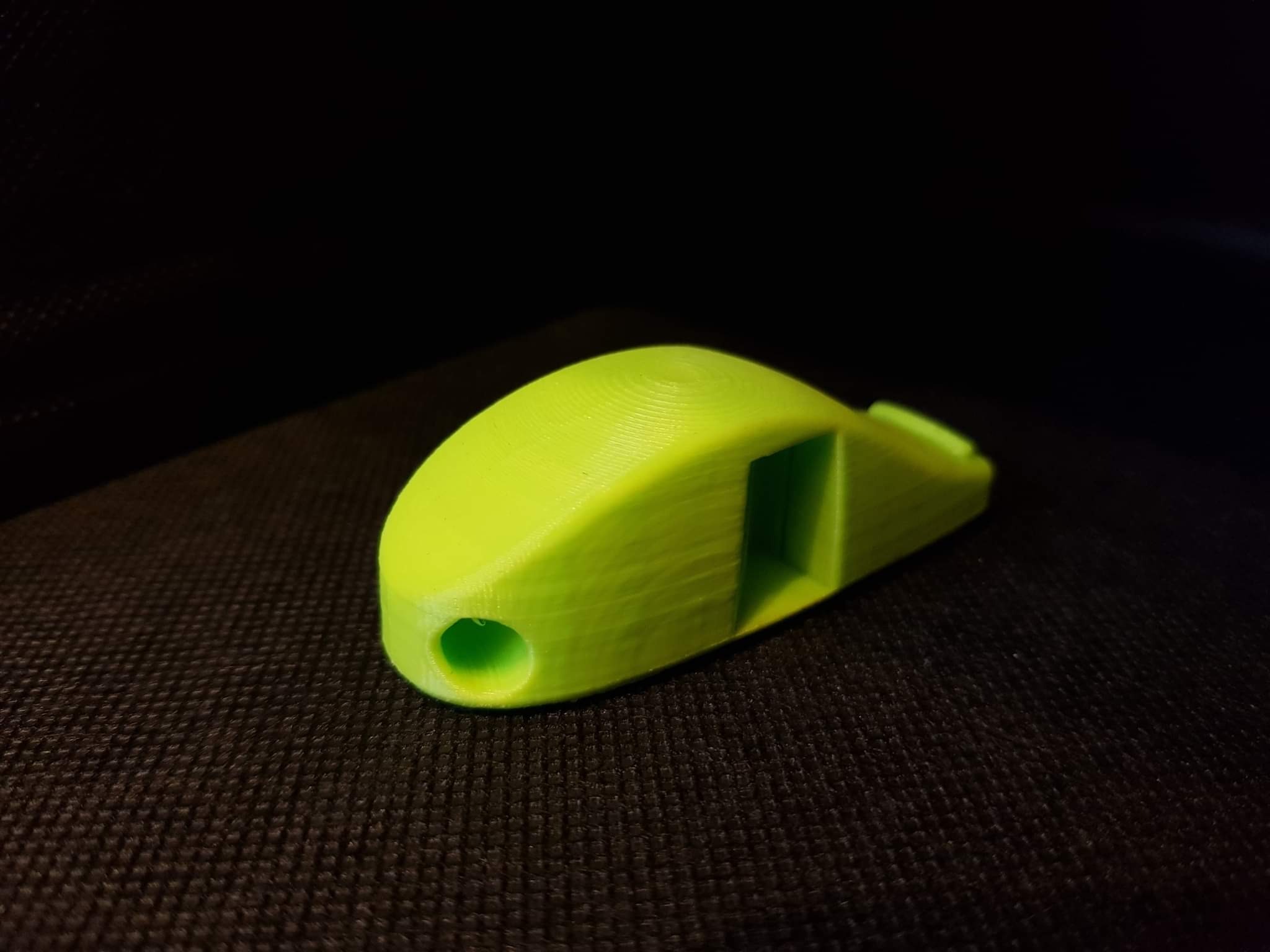 Żółty gwizdek wydrukowany w 3D, leżący na ciemnej, teksturowanej powierzchni, widoczne warstwy druku.