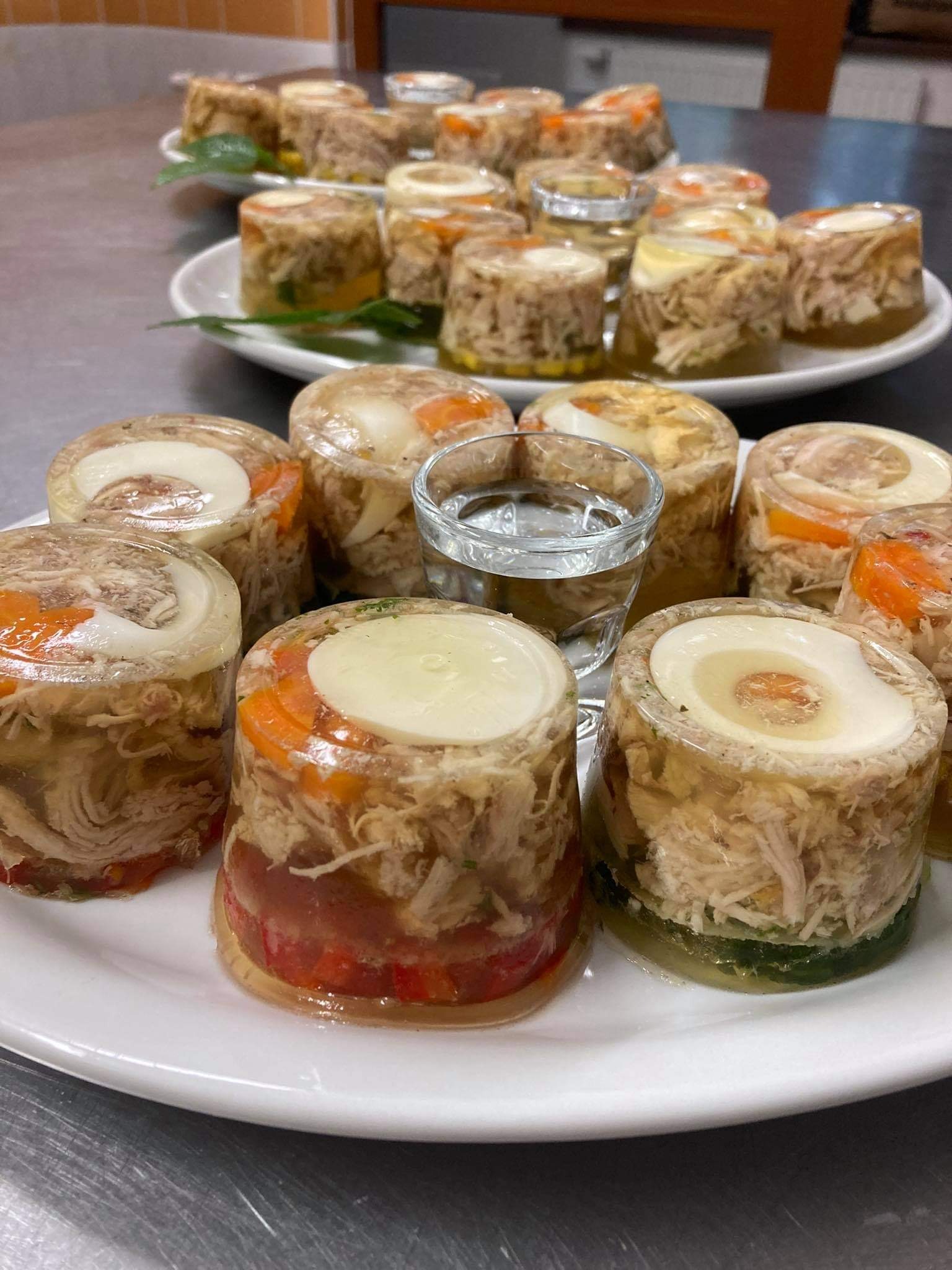 Galaretki z mięsem i warzywami, ułożone na białym talerzu, z dodatkową porcją na drugim planie, serwowane w Lubinie jako element cateringu.