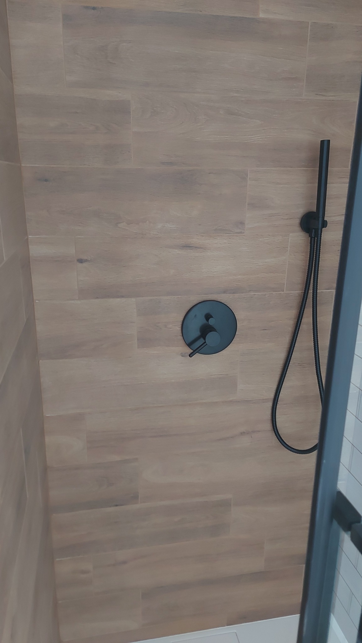 Kabina prysznicowa z brązowymi płytkami imitującymi drewno na ścianach i czarną armaturą, widok z góry.