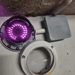 Otwarta kamera monitoringu z włączonymi diodami IR, widoczna puszka instalacyjna i przewód na szarej ścianie.