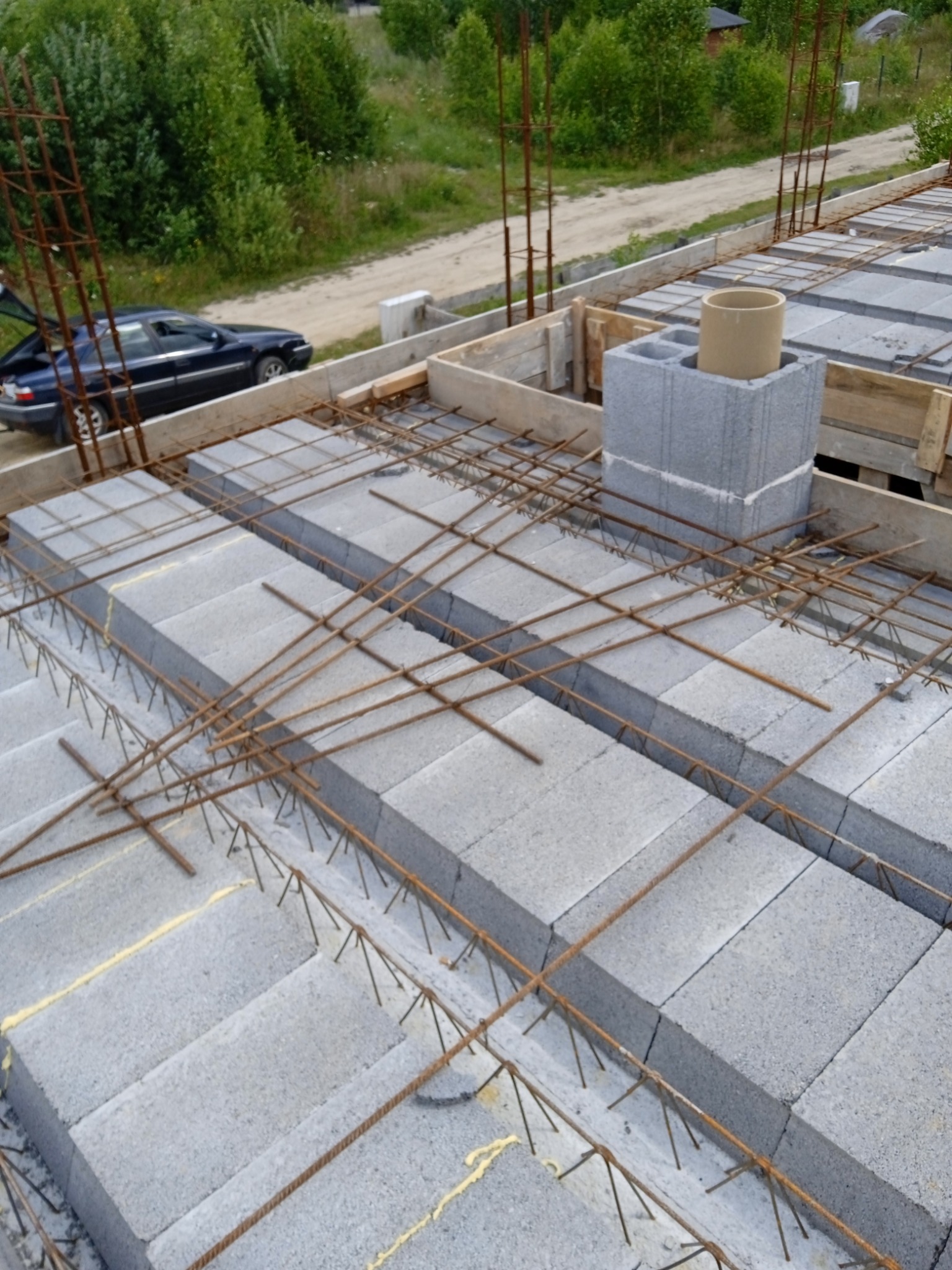 Budowa fundamentów w Kokoszkowach: szalunek z bloczków betonowych i zbrojenie stalowe przygotowane do zalania betonem, w tle widoczny samochód.