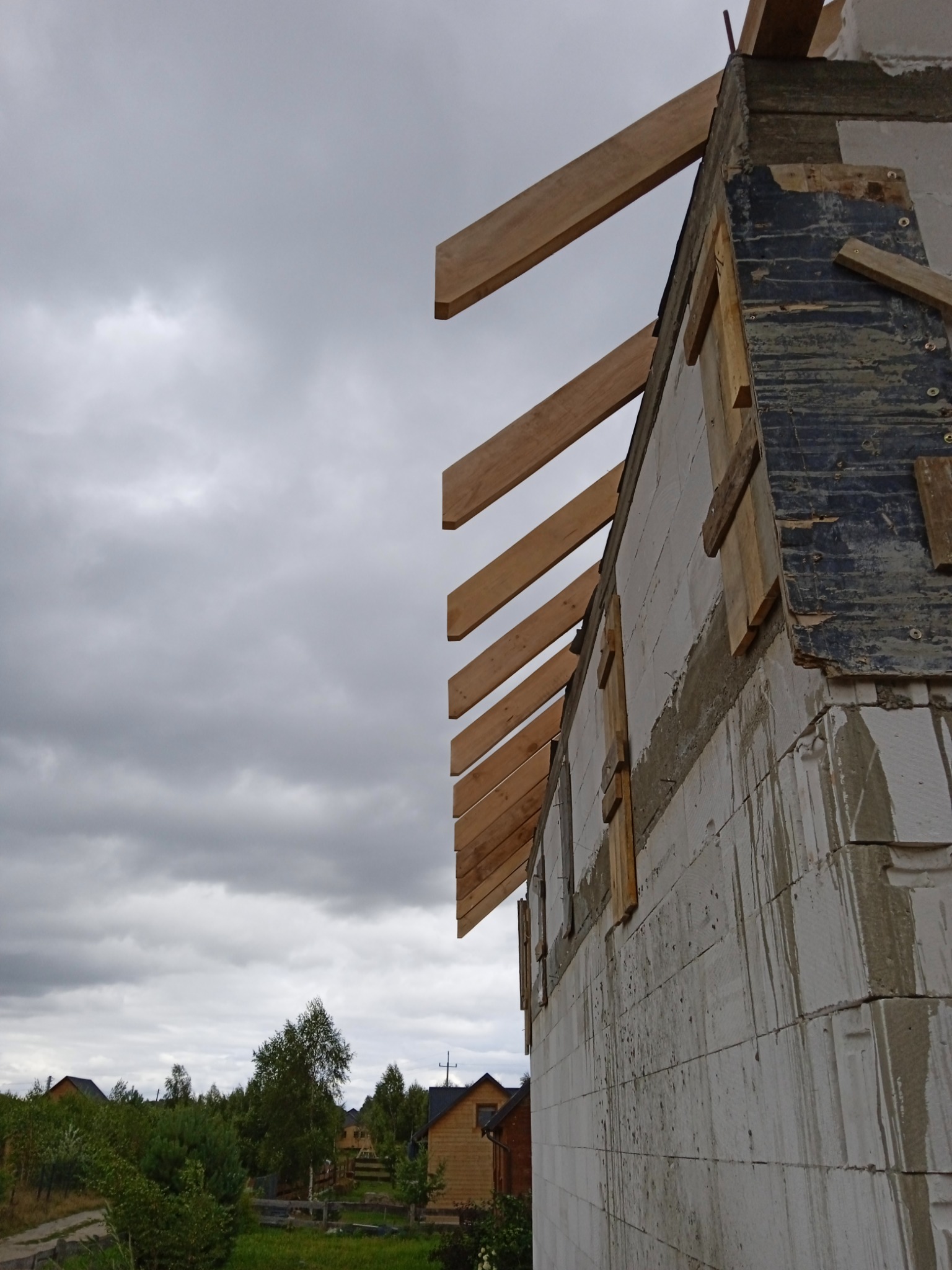 Surowy stan ściany budynku z betonu komórkowego z widocznymi śladami zaprawy i drewnianymi elementami konstrukcyjnymi, przygotowywany do dalszych prac wykończeniowych na tle pochmurnego nieba...