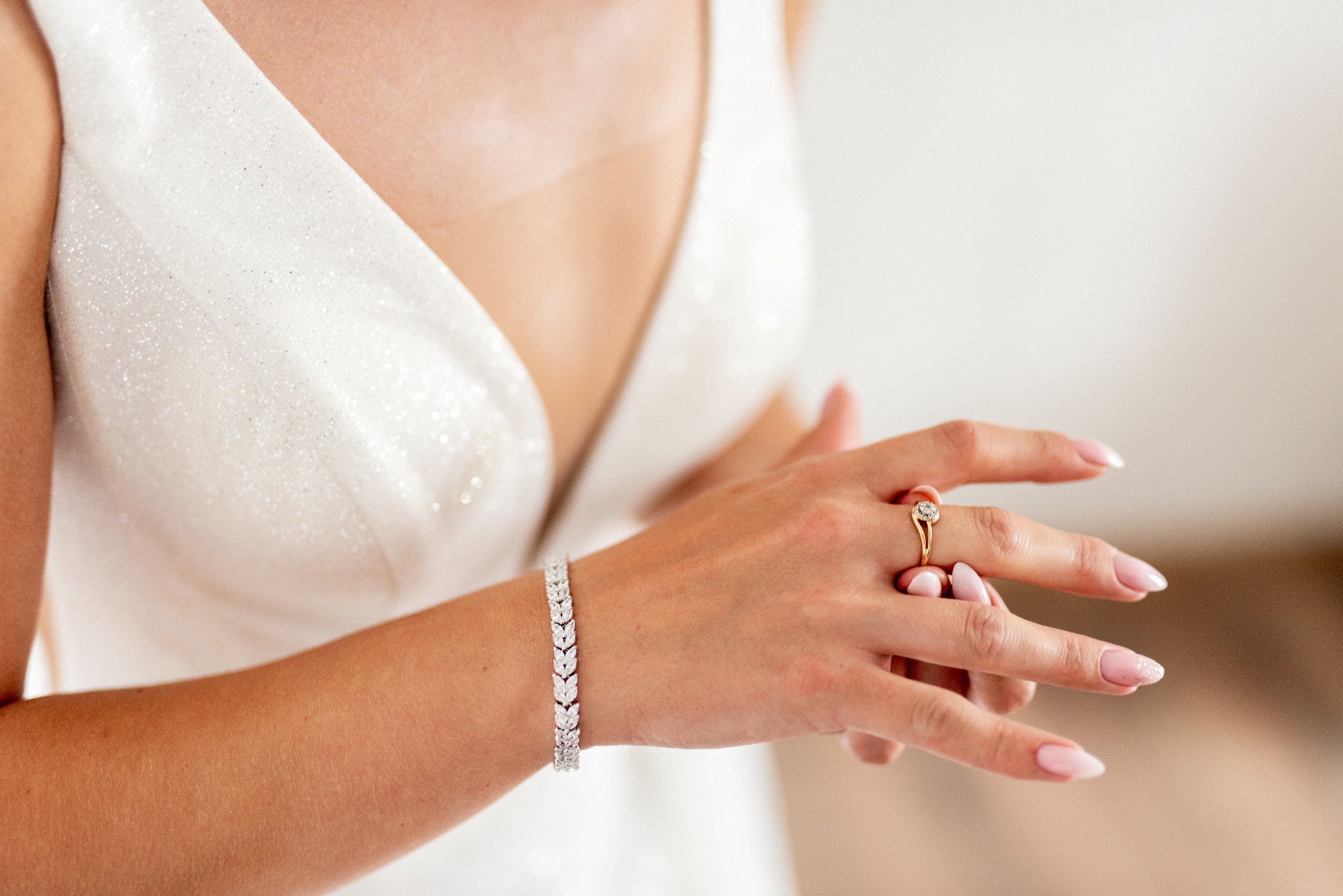 Panna młoda w Żytnie, zbliżenie na rękę z pierścionkiem zaręczynowym i bransoletką, biała suknia z delikatnym połyskiem.