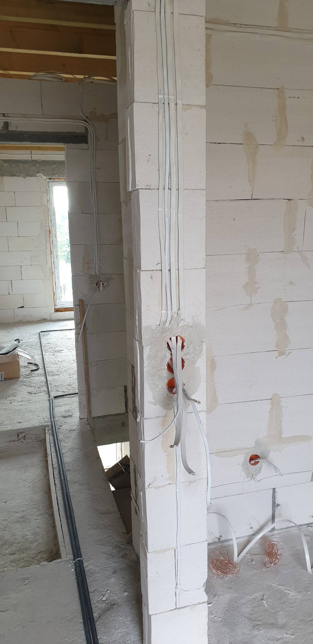Surowy stan budynku z widocznymi przewodami elektrycznymi w peszlach zamocowanymi do ściany z białych bloczków oraz puszkami instalacyjnymi w ścianie.