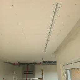 Montaż sufitu podwieszanego z płyty karton gips z widoczną konstrukcją metalową, szpachlowane łączenia płyt i lampa liniowa w przygotowanym otworze.