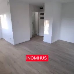 Jasne panele podłogowe w pustym, odnowionym pokoju z białymi ścianami, widok na łazienkę z kabiną prysznicową. Minimalistyczny design wnętrza.