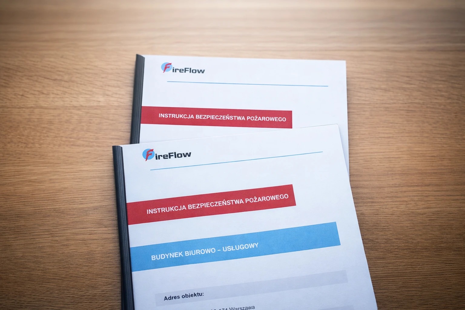 Dwie broszury FireFlow z instrukcją bezpieczeństwa pożarowego dla budynku biurowo-usługowego, leżące na drewnianym stole. Widoczny adres obiektu w Warszawie.