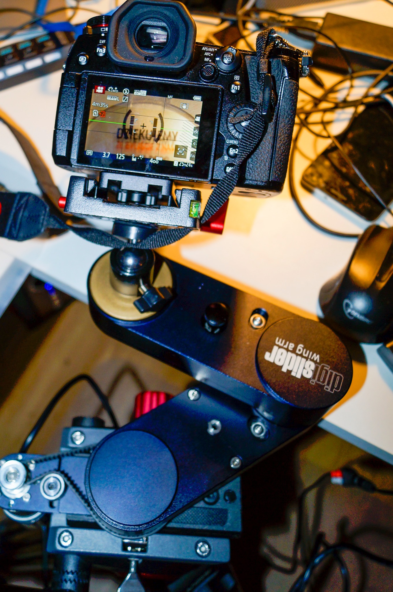 Aparat fotograficzny na sliderze DigiSlider Wing Arm, ustawiony do filmowania, widoczny ekran aparatu z ustawieniami i kadrowanym ujęciem.