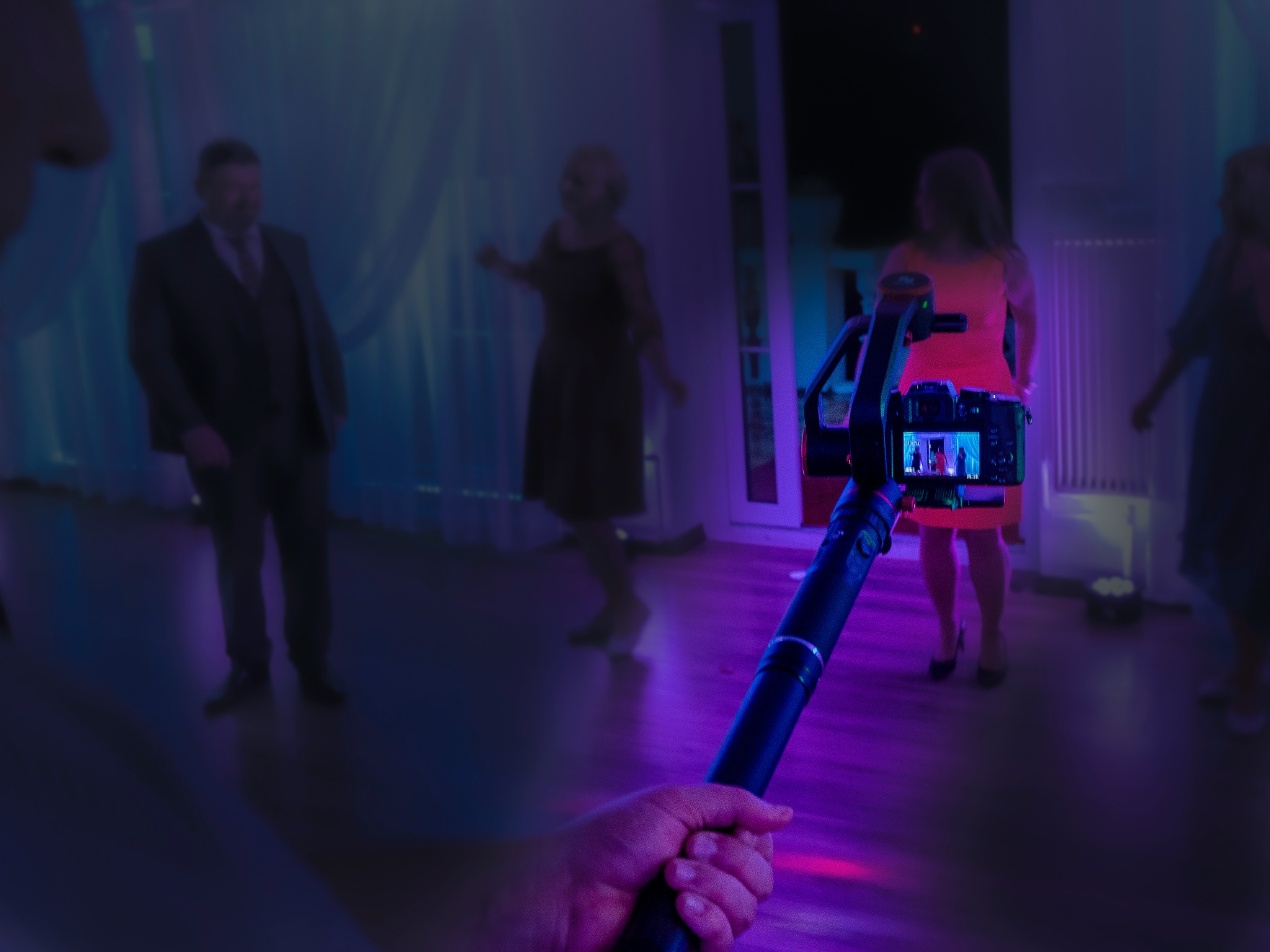 Operator filmuje tańczących gości na sali weselnej za pomocą kamery na stabilizatorze, widoczny ekran kamery z podglądem na żywo.