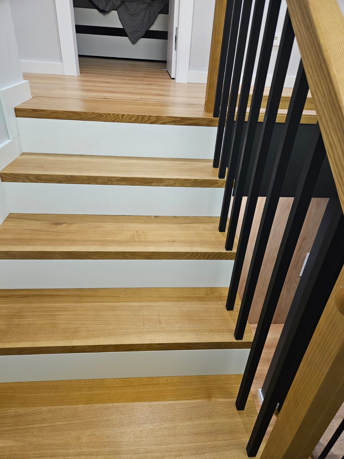 Nowoczesne schody z drewna i czarnymi balustradami w Debrznie. Jasne drewno stopni kontrastuje z białymi podstopnicami, a czarne elementy dodają elegancji.