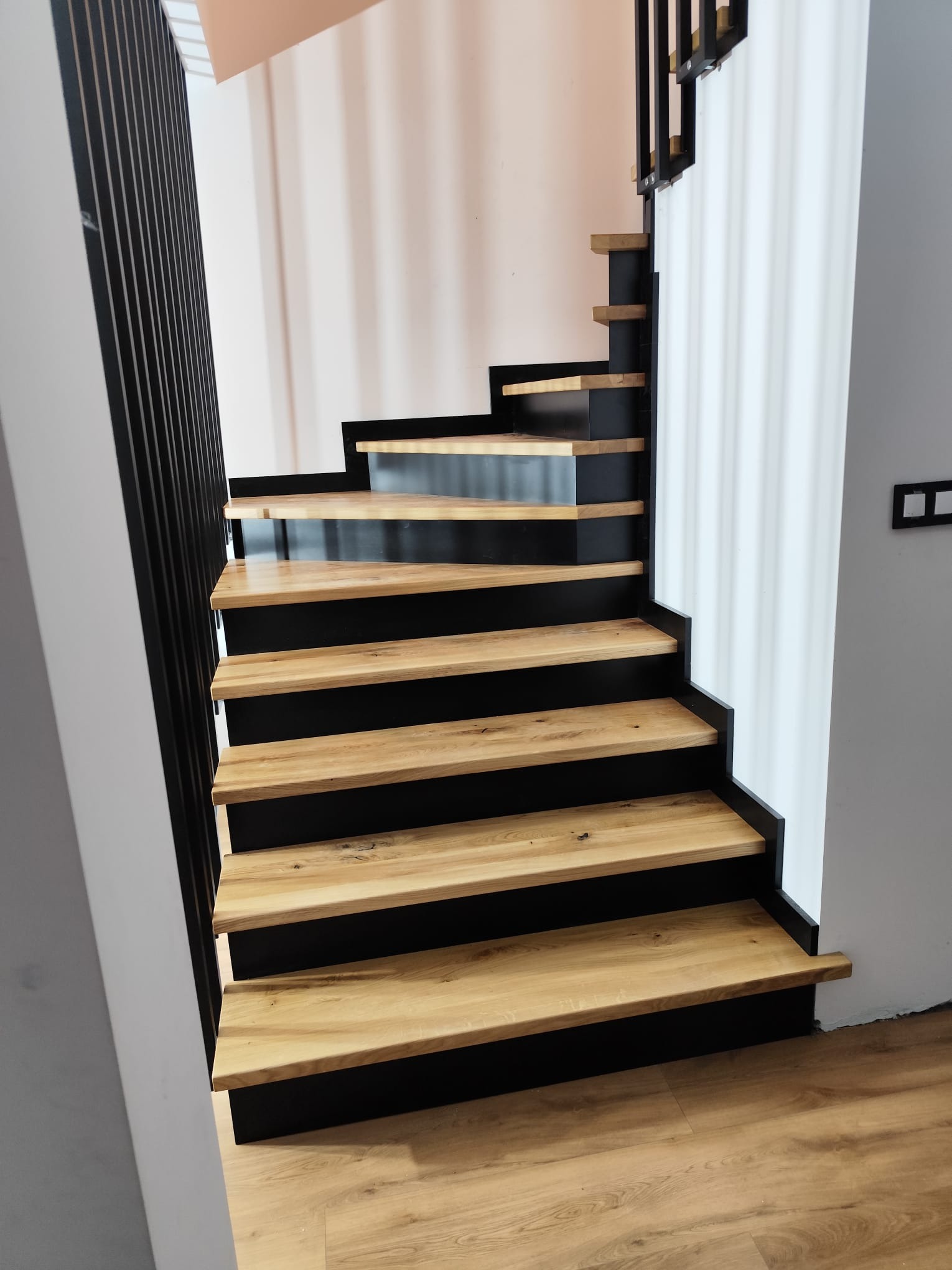 Nowoczesne schody drewniane z czarnymi podstopnicami i balustradą, widok z dołu, jasne drewno, minimalistyczny design, oświetlenie naturalne.