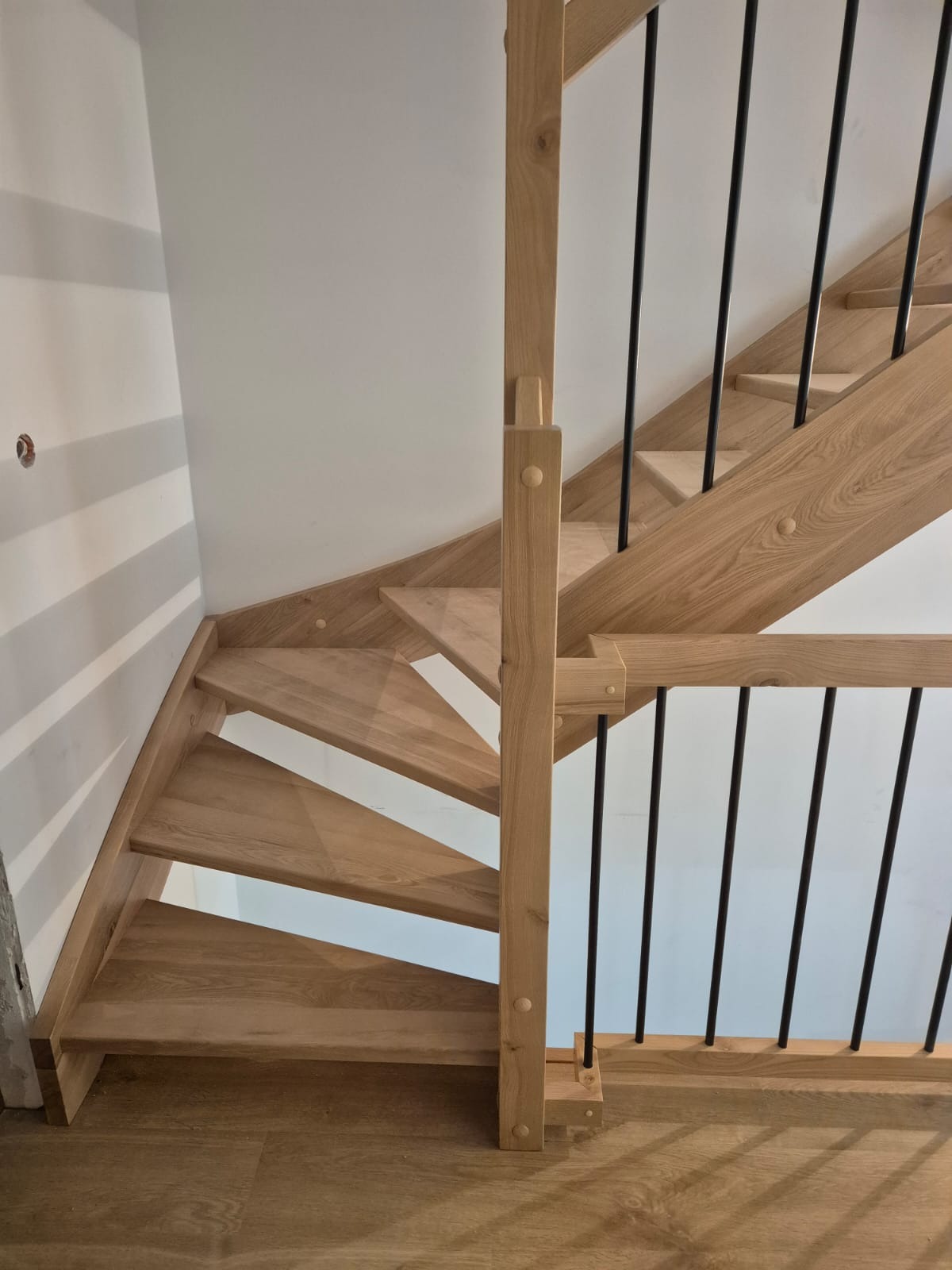 Drewniane schody z czarnymi metalowymi balustradami, widok z dołu, jasne drewno, minimalistyczny design, nowoczesne wykończenie.