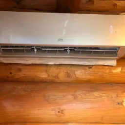 Zamontowany klimatyzator Cooper&Hunter z widocznym wyświetlaczem temperatury, zainstalowany na ścianie z bali drewnianych w domu całorocznym.