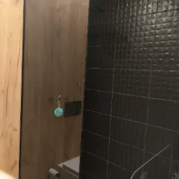 Nowoczesna łazienka z czarnymi trójwymiarowymi płytkami, kabiną prysznicową typu walk-in i elementami drewnopodobnymi.