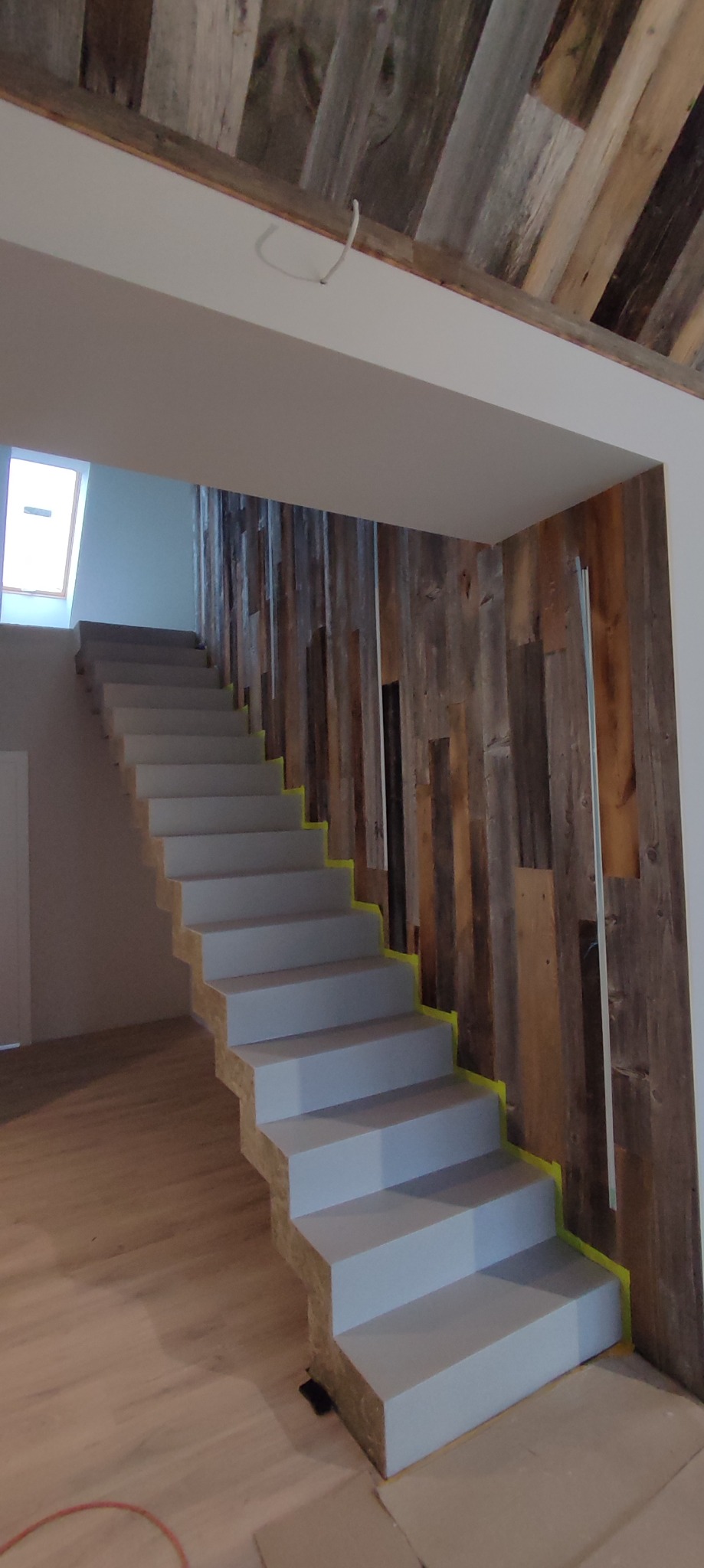 Schody w trakcie malowania, zabezpieczone taśmą malarską, z drewnianą ścianą w tle i drewnianym sufitem z recyklingu.