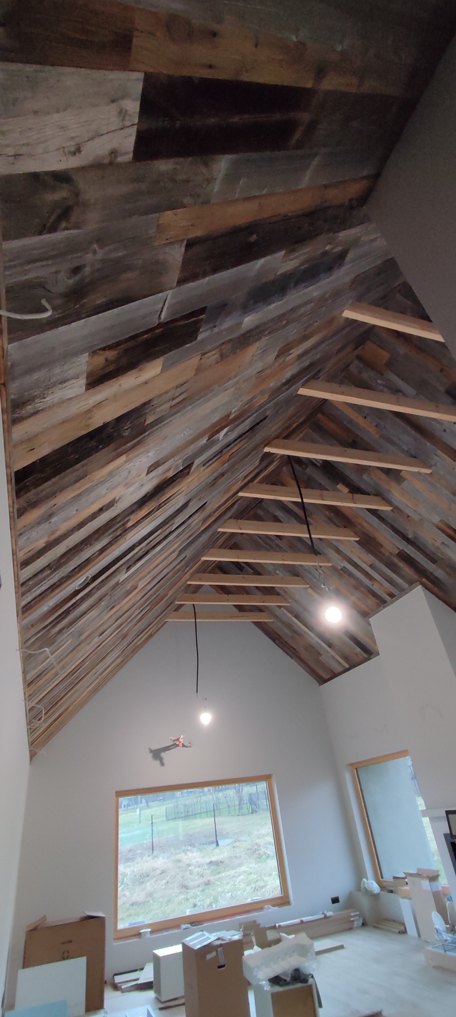 Skośny sufit wykończony panelami z postarzanego drewna, widoczne elementy konstrukcyjne i wiszące przewody oświetleniowe, wnętrze w trakcie prac wykończeniowych.