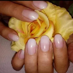 Dłonie prezentują subtelny, ombre manicure w odcieniach bieli i różu, na tle rozkwitającego, żółtego kwiatu.