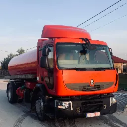 Czerwona cysterna na podwoziu ciężarówki, zaparkowana w Morawicy na tle domu jednorodzinnego, widoczne ślady opon na asfalcie.