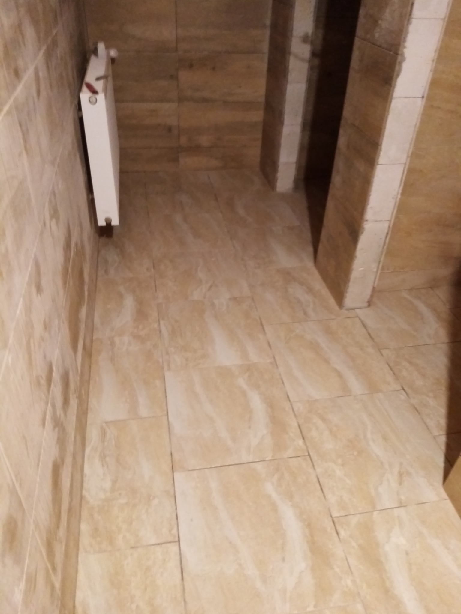 Beżowe płytki podłogowe i ścienne w łazience z grzejnikiem na ścianie, widok z góry