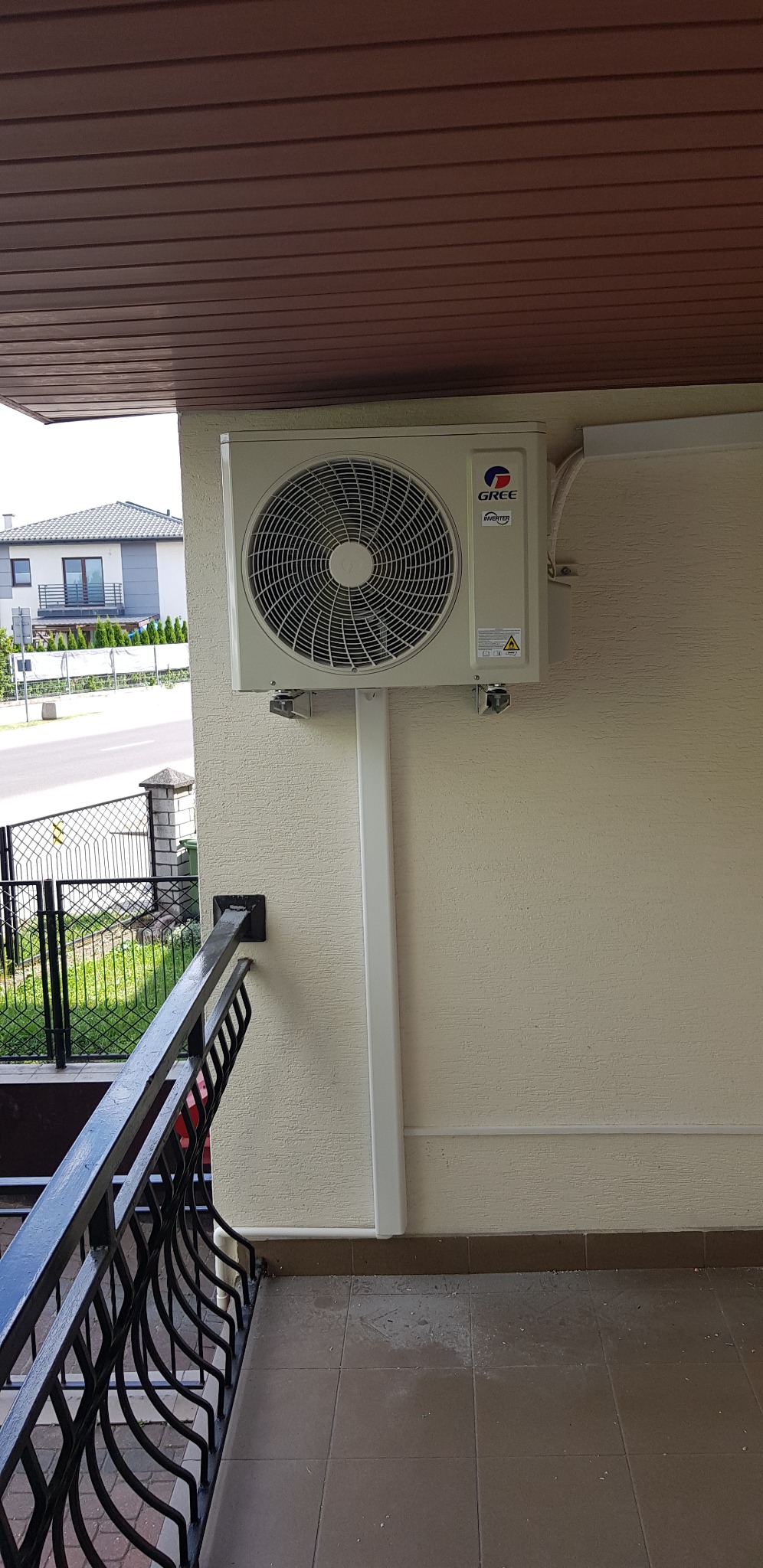 Zewnętrzna jednostka klimatyzacji marki Gree zamontowana na balkonie budynku mieszkalnego, widoczne elementy instalacji i fragment otoczenia.