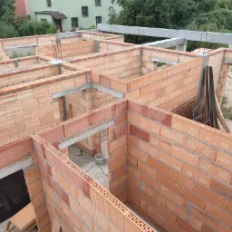 Wznoszenie ścian z czerwonej ceramiki poryzowanej, widok z góry na budowę domu jednorodzinnego, zbrojenie pionowe w narożnikach, betonowe nadproża.