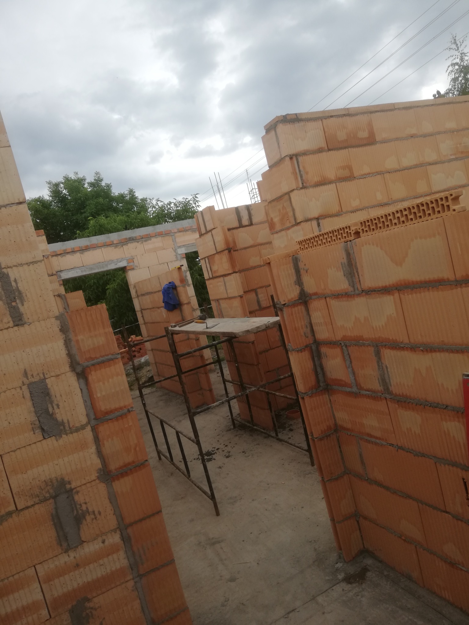 Wznoszone ściany domu z cegieł ceramicznych, widoczny rusztowanie i niebieska torba robocza, etap budowy z surowym stanem budynku