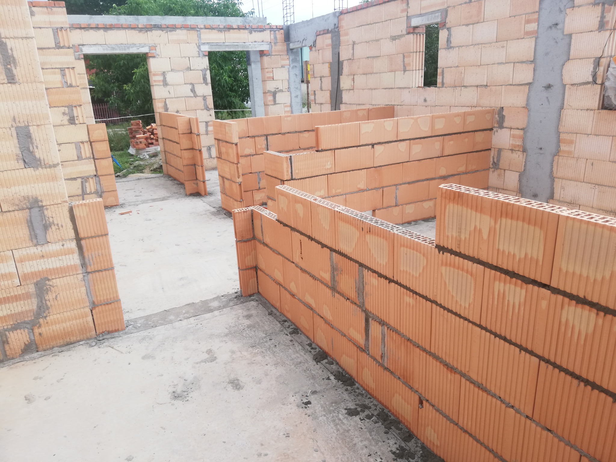 Wznoszenie ścian wewnętrznych z bloczków ceramicznych Porotherm na zaprawie cementowej, widoczne otwory okienne i drzwiowe w trakcie budowy domu.