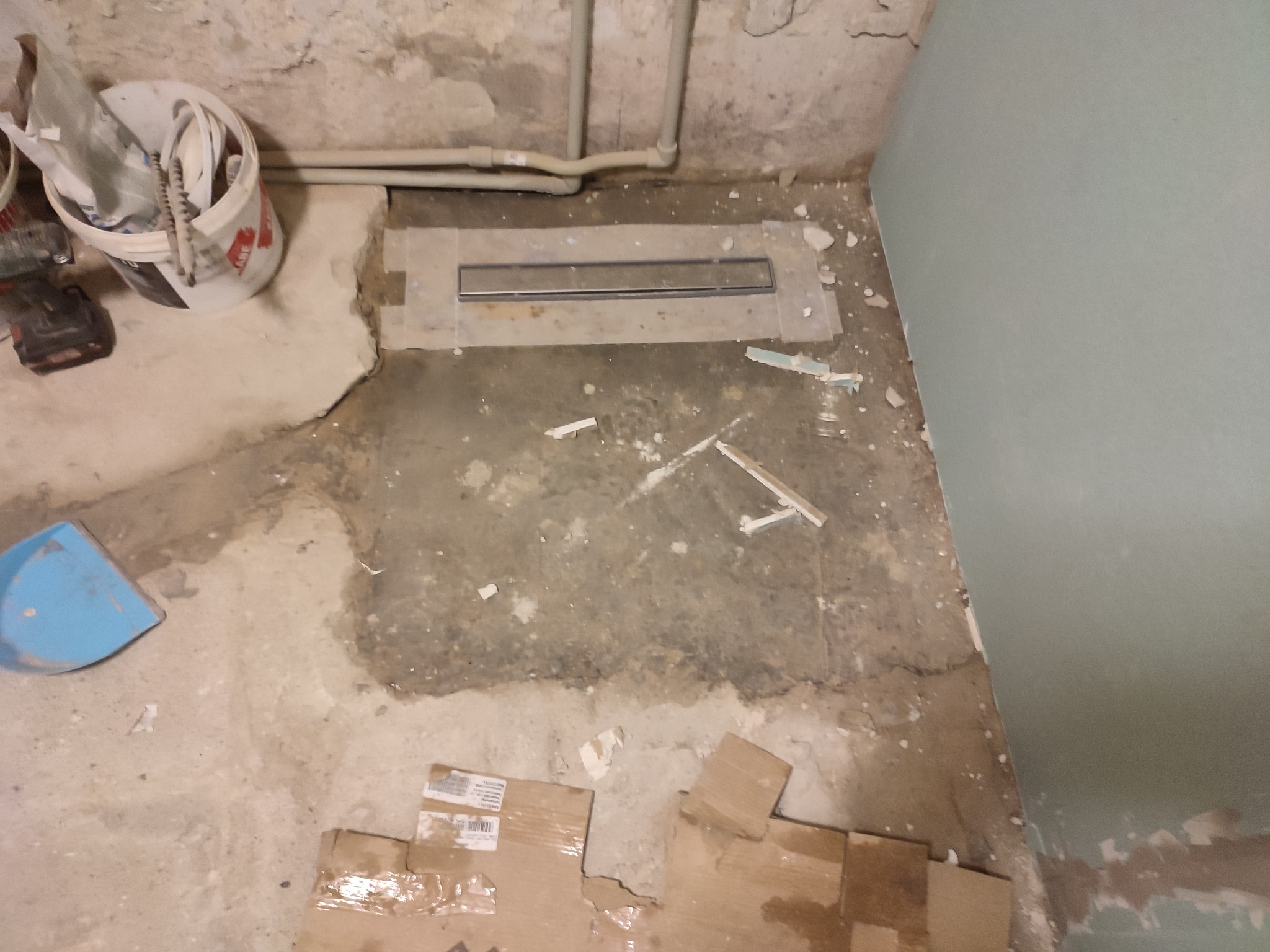 Montaż odpływu liniowego w posadzce łazienki w Połajewie, widoczne narzędzia i materiały budowlane.