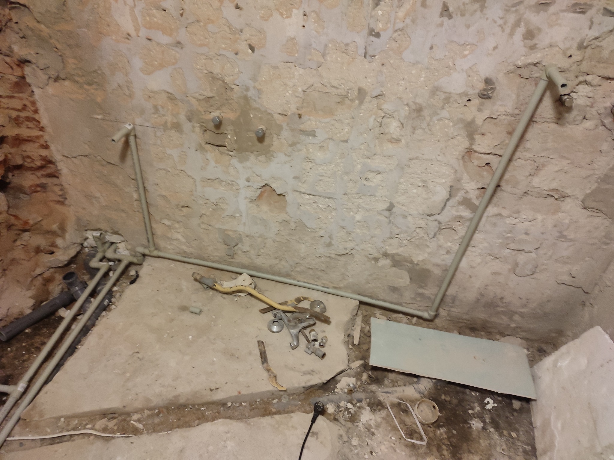 Surowe ściany z kamienia w trakcie instalacji rur wodociągowych, widoczne narzędzia i elementy instalacyjne na podłodze.