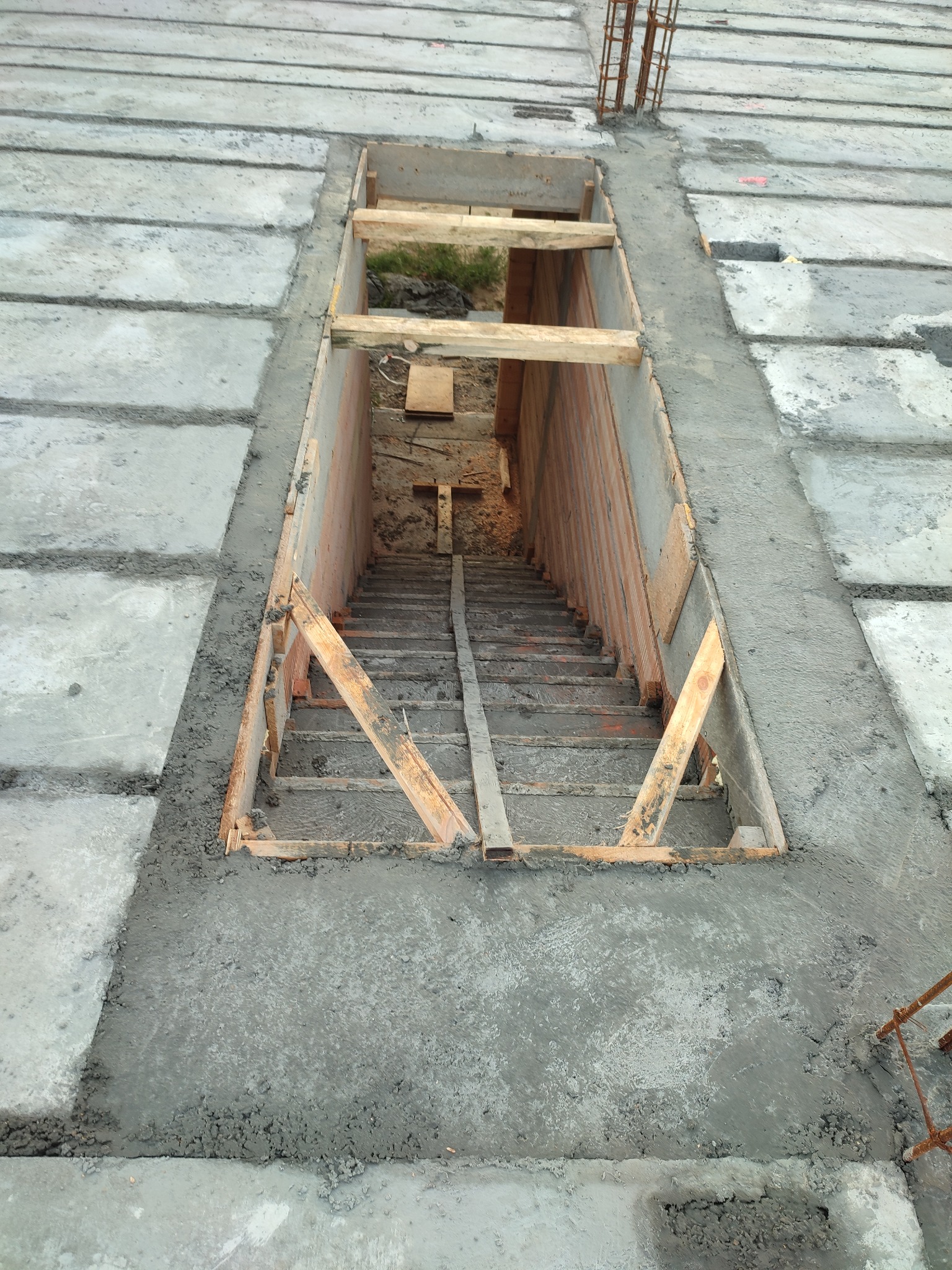 Wykop pod schody w surowym betonowym stropie, drewniane szalunki i zbrojenia widoczne.