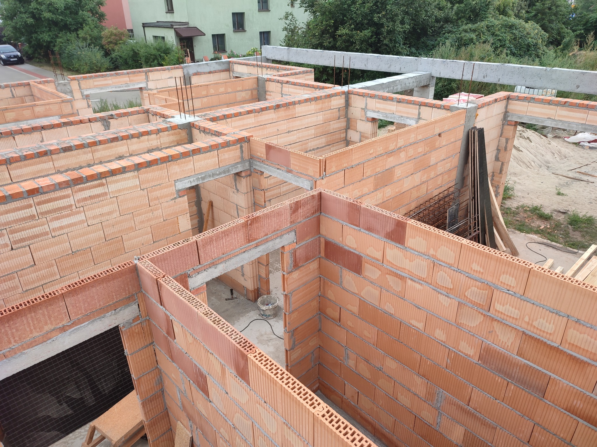 Wznoszenie ścian z czerwonej ceramiki poryzowanej, widok z góry na budowę domu jednorodzinnego, zbrojenie pionowe w narożnikach, betonowe nadproża.