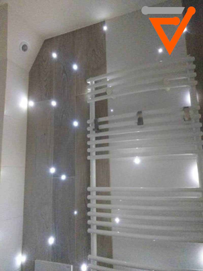 Nowoczesna łazienka z punktowym oświetleniem LED w ścianie z imitacją drewna i białym grzejnikiem drabinkowym.