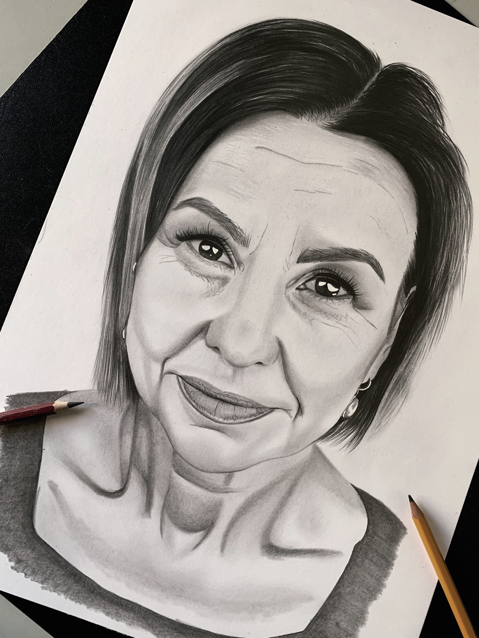 Szkic ołówkiem portretu kobiety, widoczne dwa ołówki obok rysunku, jeden z czerwoną obudową, drugi żółty.