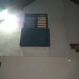 Nocne ujęcie fragmentu elewacji budynku w Białymstoku z oknem zabezpieczonym poziomą, metalową konstrukcją, prawdopodobnie balkonową, oświetloną jasnym światłem z g&oacute;ry.