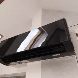 Czarny klimatyzator marki Gree zamontowany na ścianie w pomieszczeniu ze skośnym sufitem i drewnianymi belkami stropowymi.