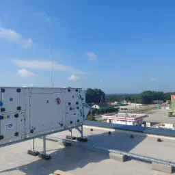 Centrala wentylacyjna na dachu budynku przemysłowego, z widocznym logo CIC Jan Hrebec i elementami instalacji w osłonach, na tle błękitnego nieba i zabudowań Rockwool.