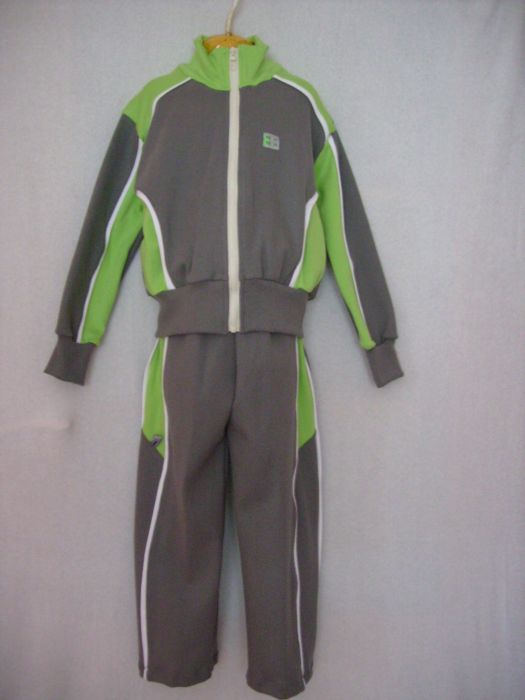 Szaro-zielony dres dziecięcy na wieszaku, z białymi lampasami i małym logo na bluzie.