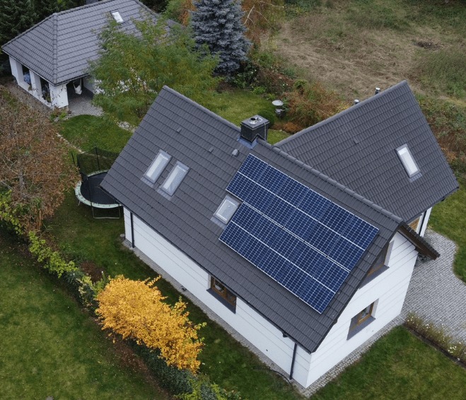 Widok z góry na dom z panelami słonecznymi na dachu i trampoliną w ogrodzie.
